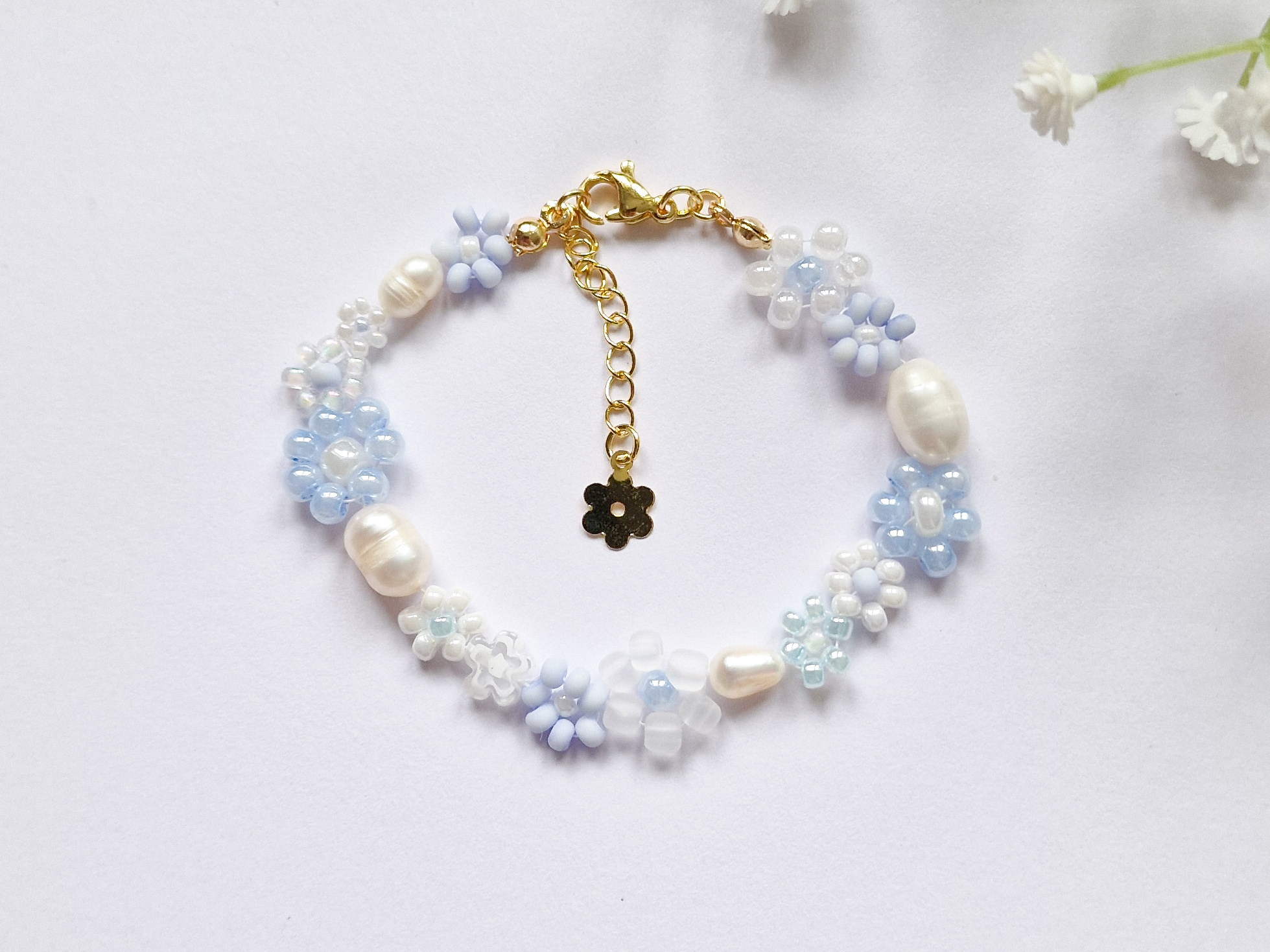 Håndlaget perlearmbånd med blomster i blått og hvitt. Seed beads, ferskvannsperler og gullforgylt lås.
