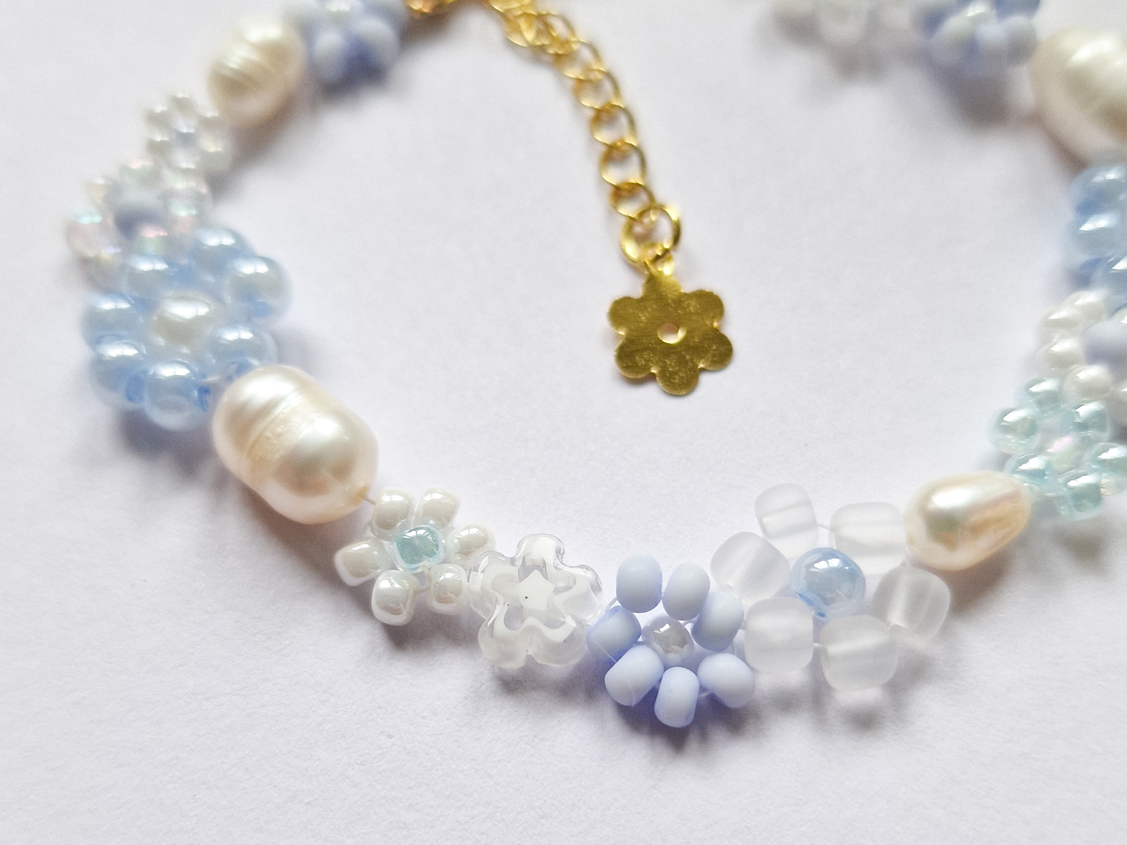 Håndlaget perlearmbånd med blomster i blått og hvitt. Seed beads, ferskvannsperler og gullforgylt lås.