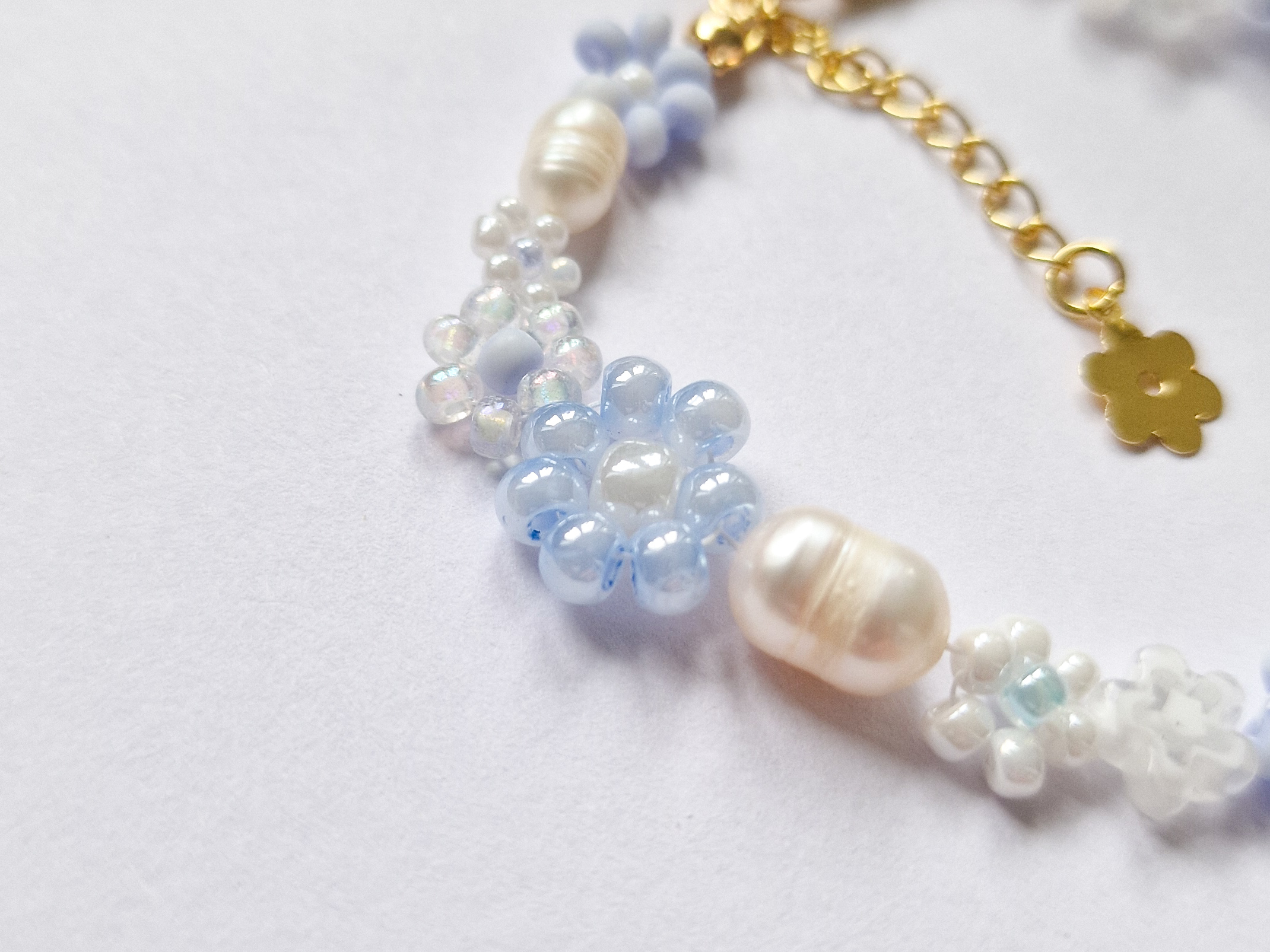 Håndlaget perlearmbånd med blomster i blått og hvitt. Seed beads, ferskvannsperler og gullforgylt lås.