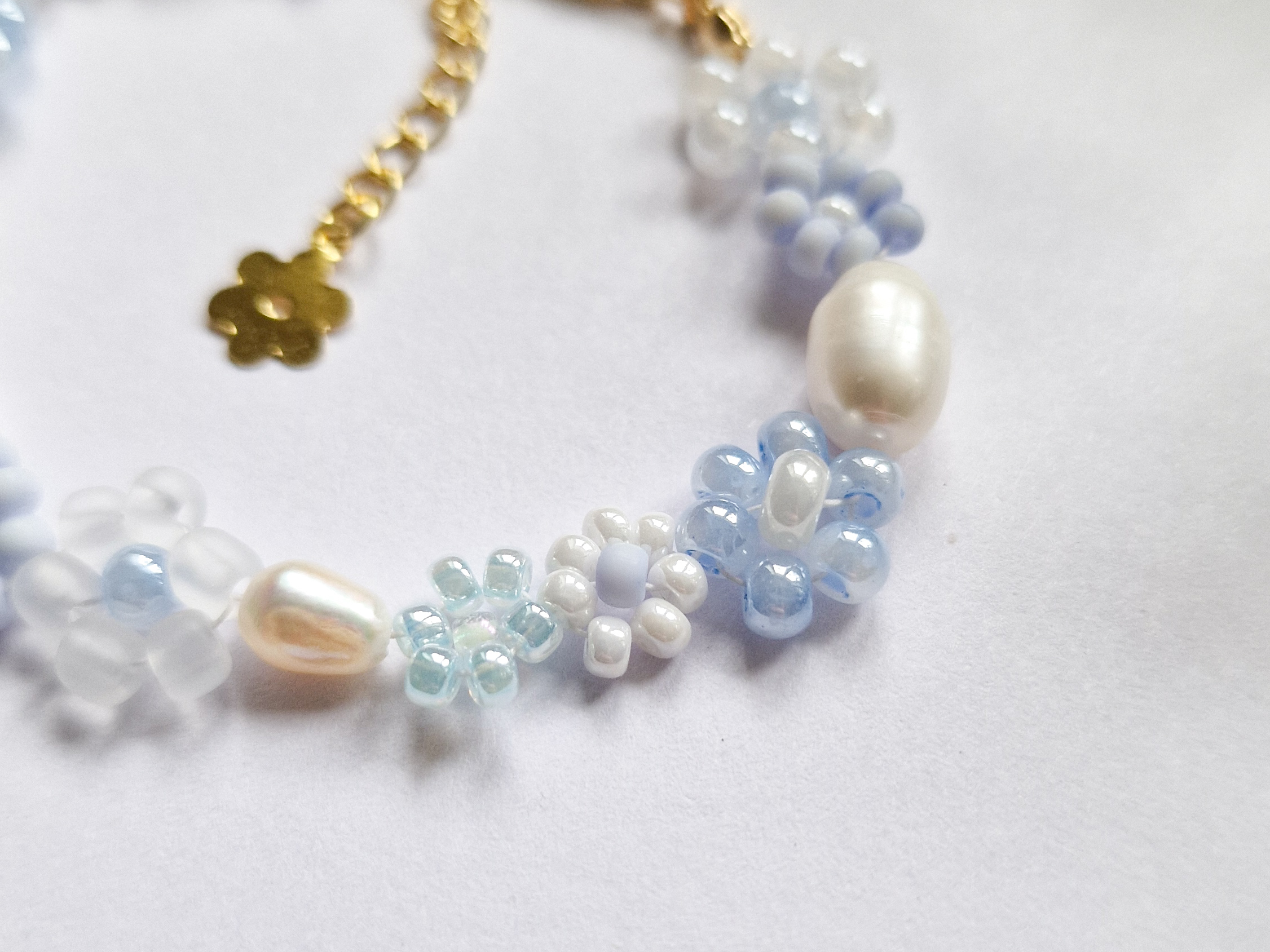 Håndlaget perlearmbånd med blomster i blått og hvitt. Seed beads, ferskvannsperler og gullforgylt lås.