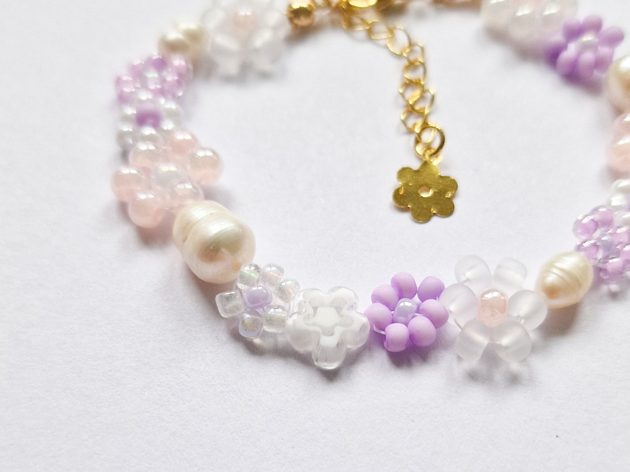Håndlaget perlearmbånd med blomster i lilla, rosa og hvitt. Seed beads, ferskvannsperler og gullforgylt lås.