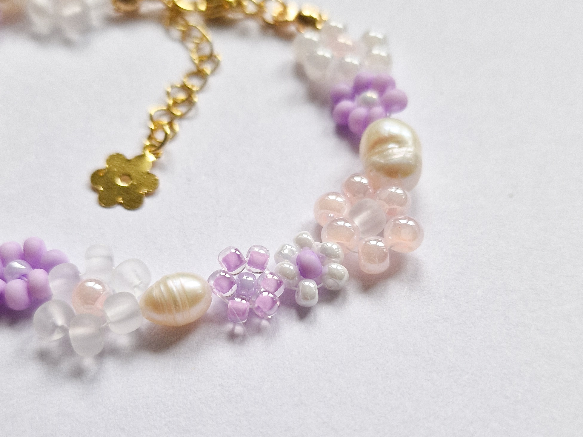 Håndlaget perlearmbånd med blomster i lilla, rosa og hvitt. Seed beads, ferskvannsperler og gullforgylt lås.