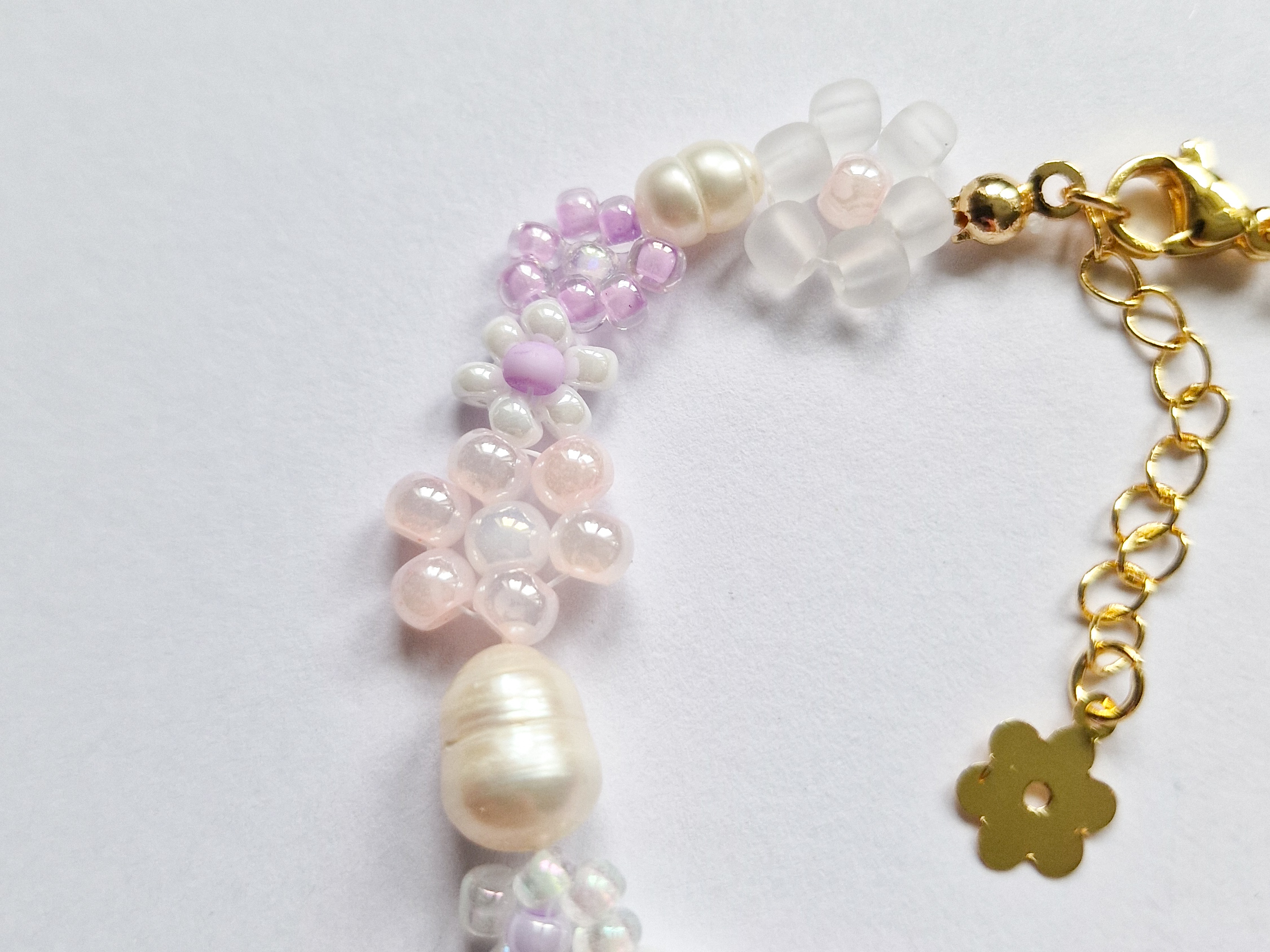 Håndlaget perlearmbånd med blomster i lilla, rosa og hvitt. Seed beads, ferskvannsperler og gullforgylt lås.