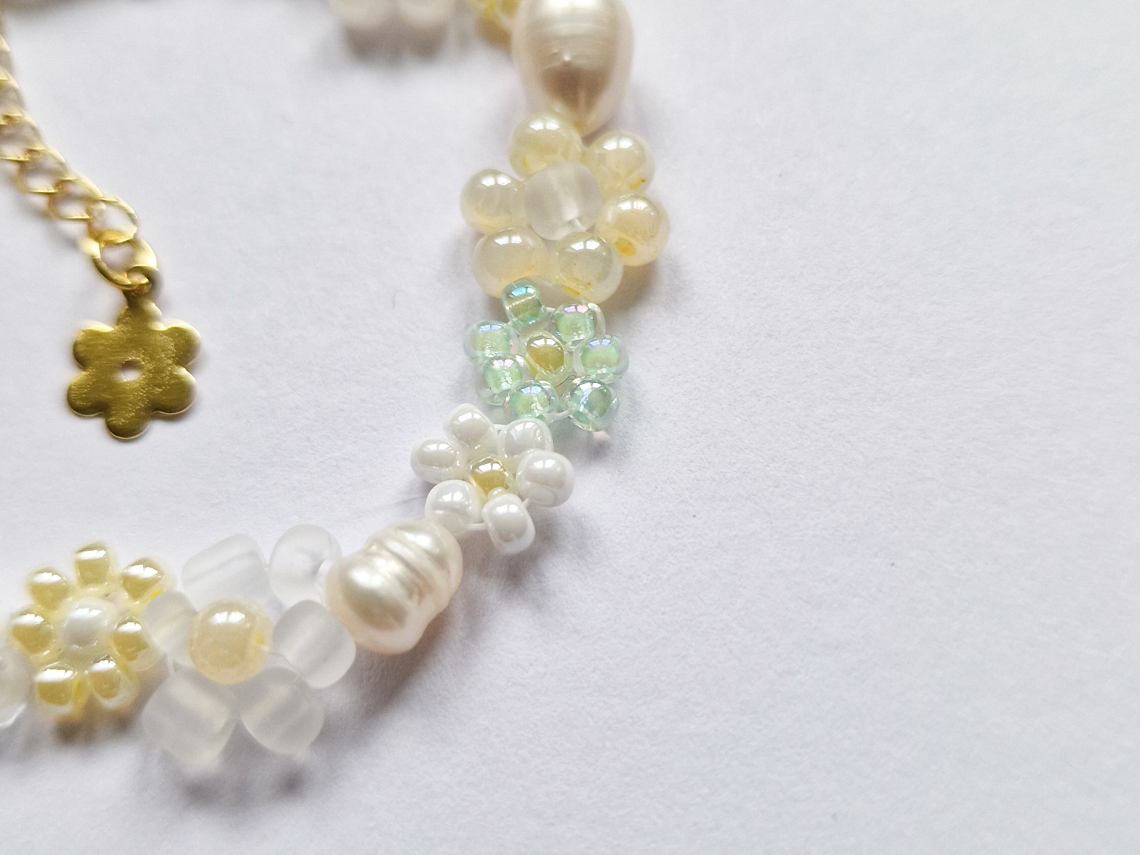 Håndlaget perlearmbånd med blomster i gult, grønt og hvitt. Seed beads, ferskvannsperler og gullforgylt lås.